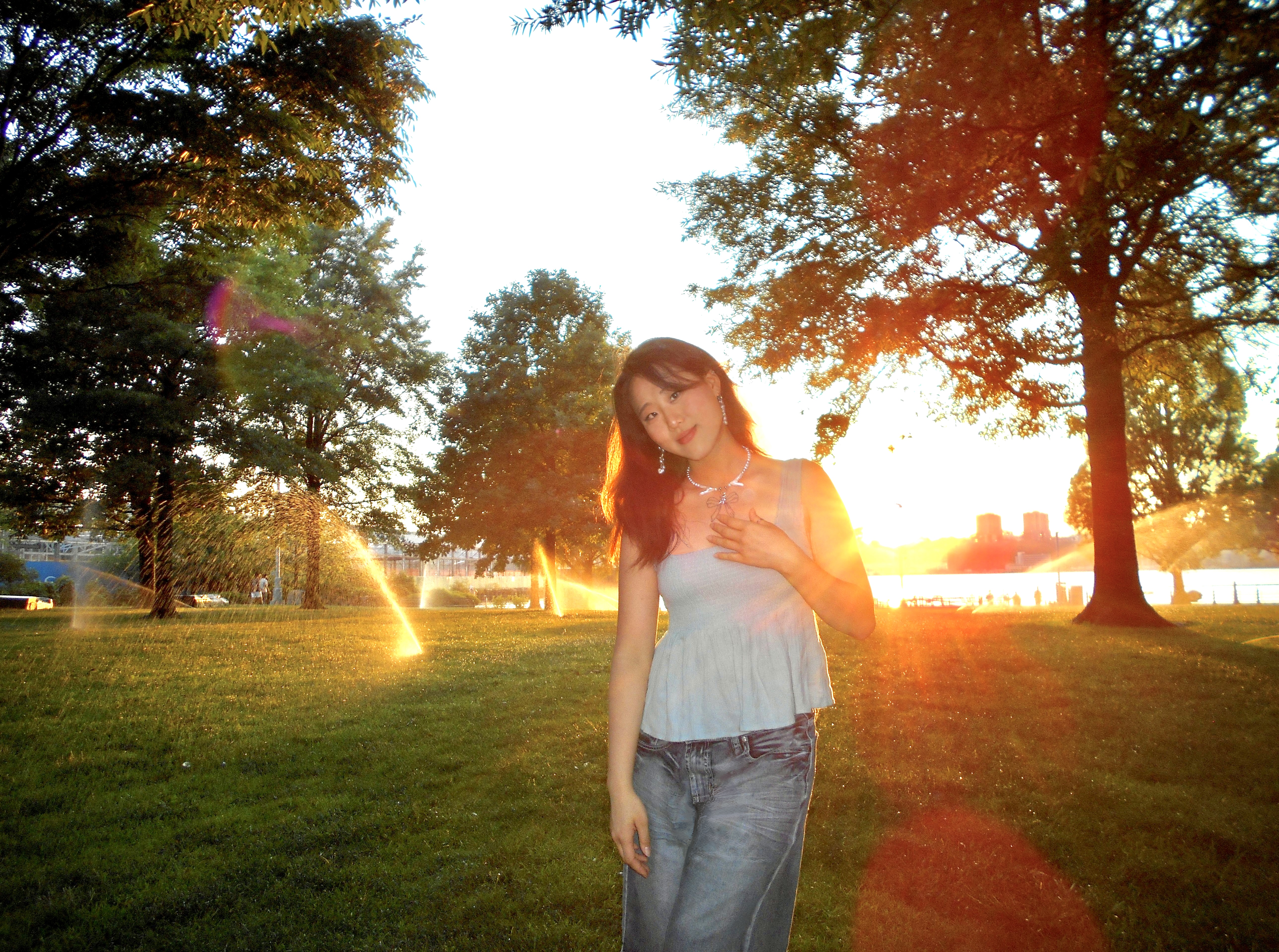 Person standing in a park at sunset, with sunlight flaring through the trees.