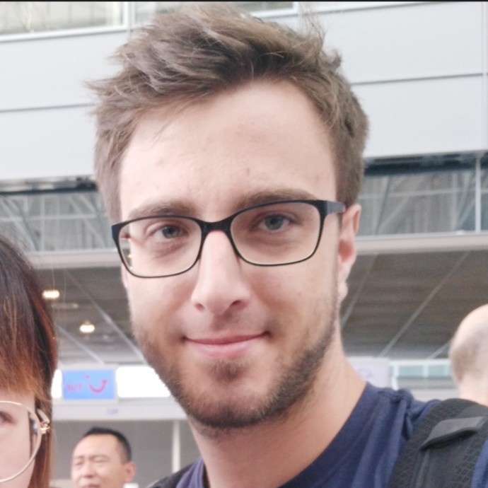 Close-up portrait of a smiling individual with glasses, wearing a dark blue shirt.