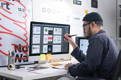 Man working at a computer, wireframes for a digital design project are visible on the screen